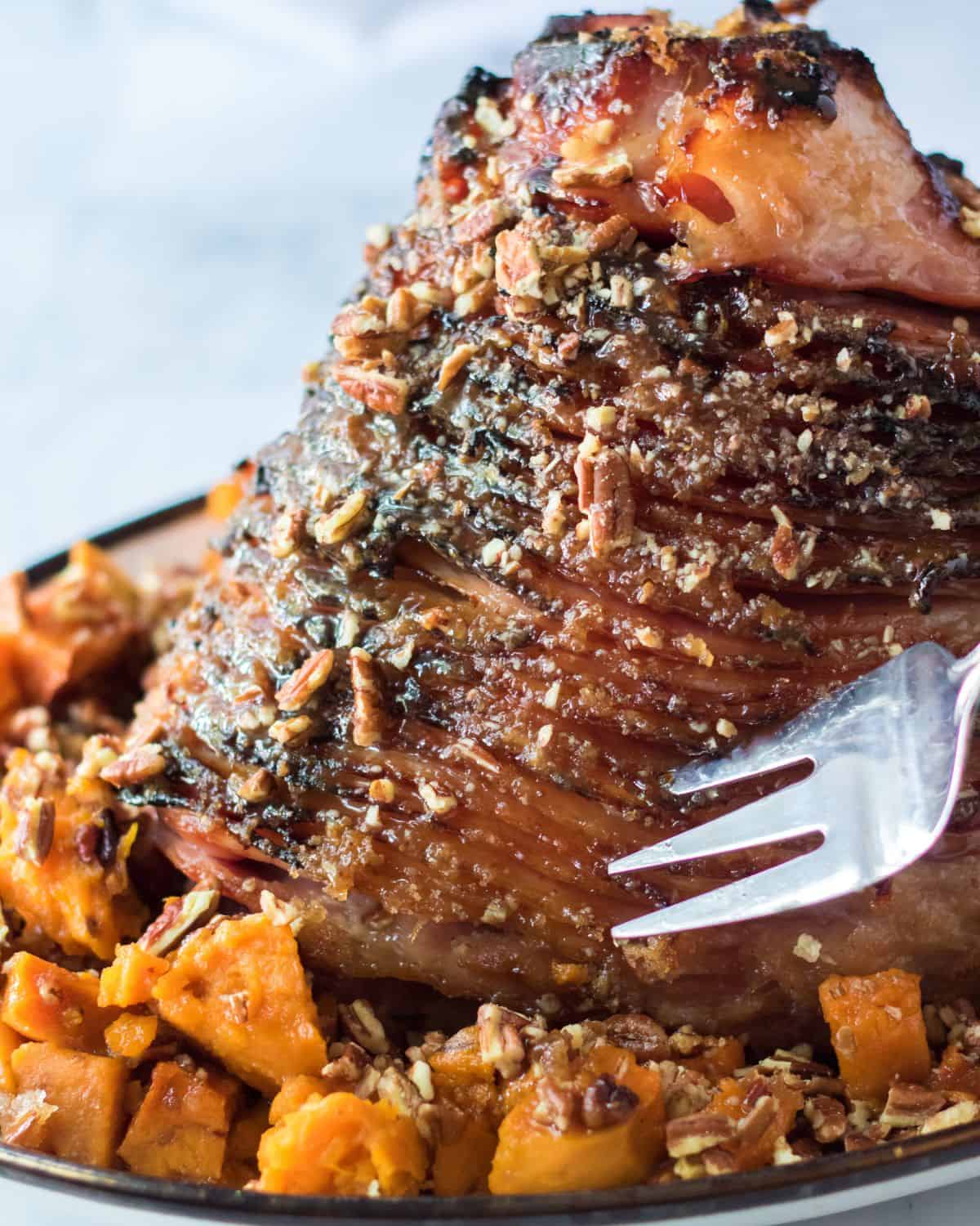 Pecan Glazed Baked Ham with sweet potatoes in a large baking dish.