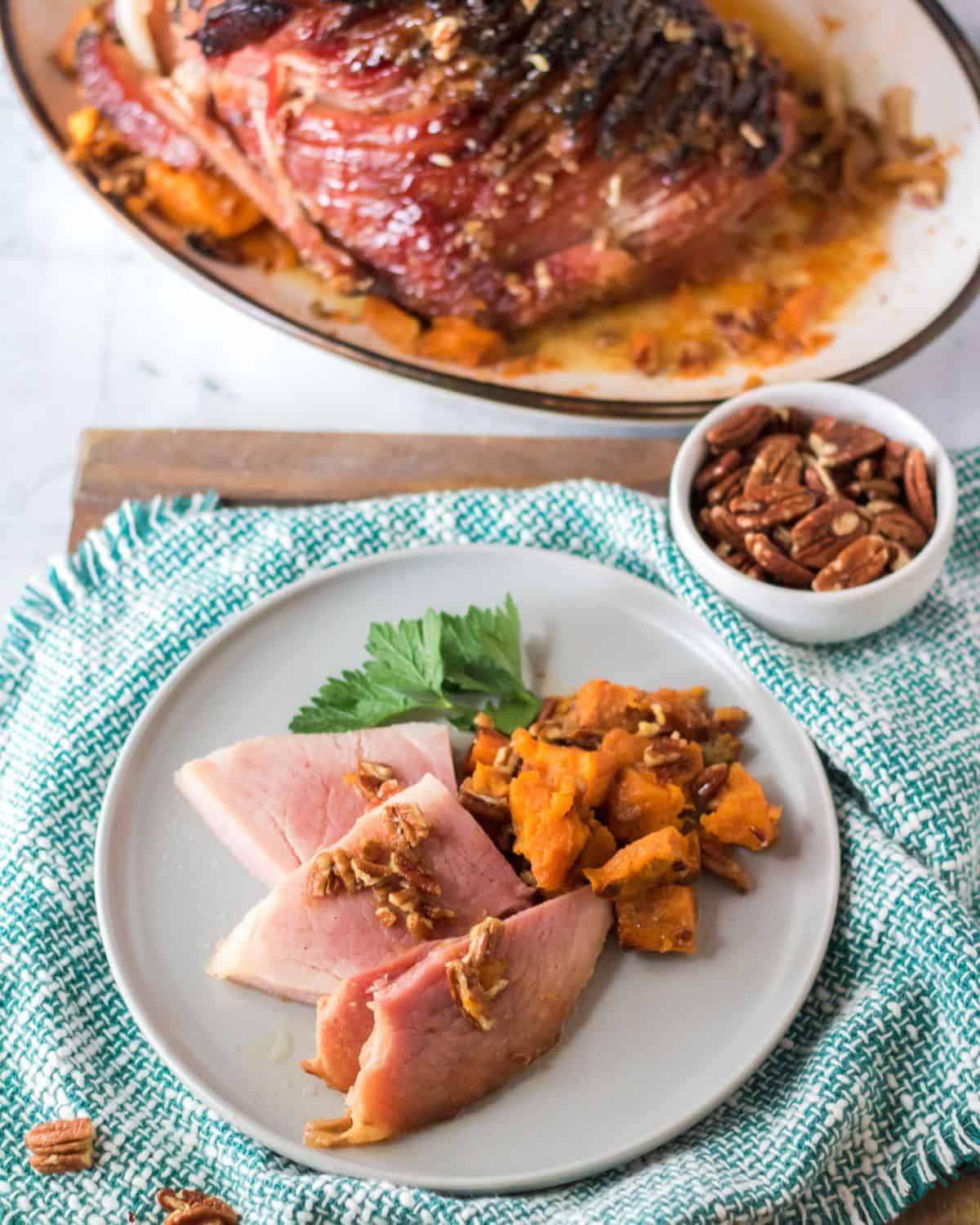 Sliced ham that has been baked in a pecan glaze on a plate with sweet potatoes. 