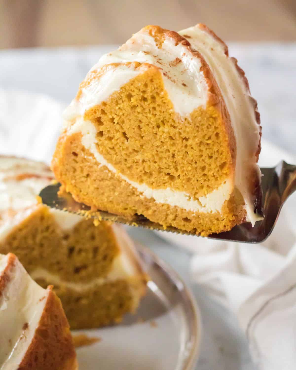 A slice of bundt cake with a cream cheese swirl on a serving knife being taken from the pumpkin bundt cake.