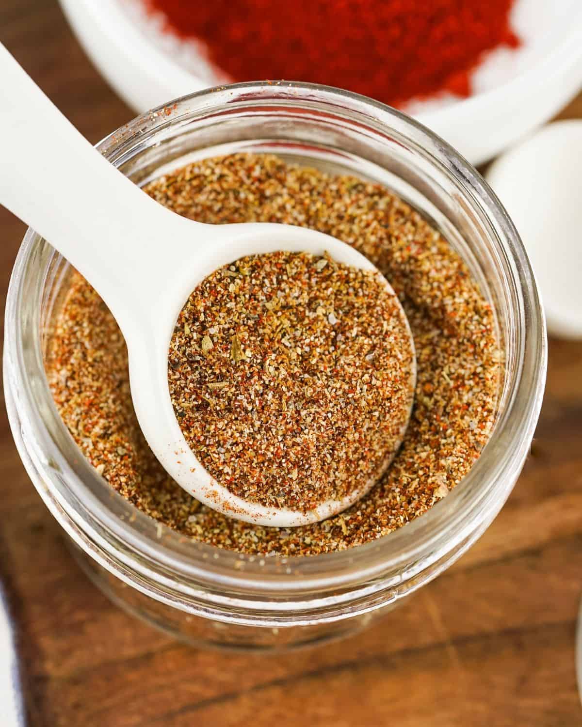 A mason jar filled with taco seasoning with a white spoon pulling out some of the seasoning.