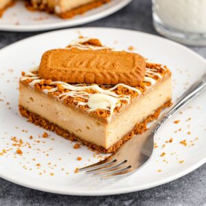 A slice of cheesecake with biscoff cookie butter cream cheese filling with a cookie on top of the cheesecake.