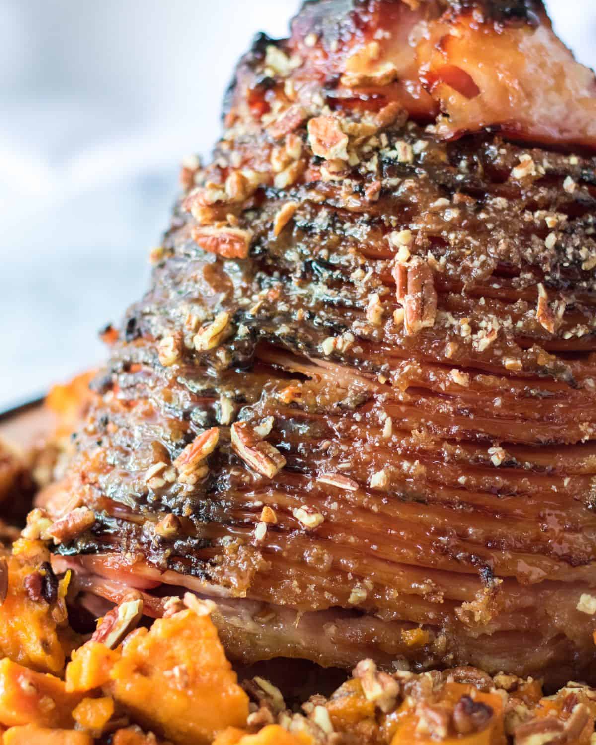 A spiral ham covered with chopped pecans and sliced sweet potatoes all around the ham.