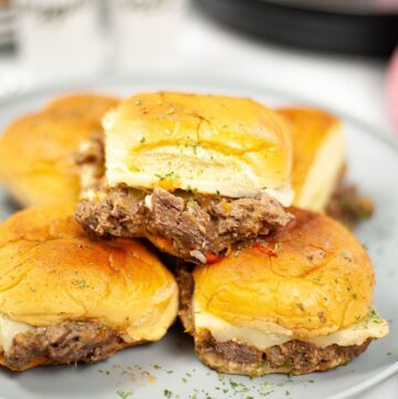 A stack of Philly cheesesteak sliders on a plate.