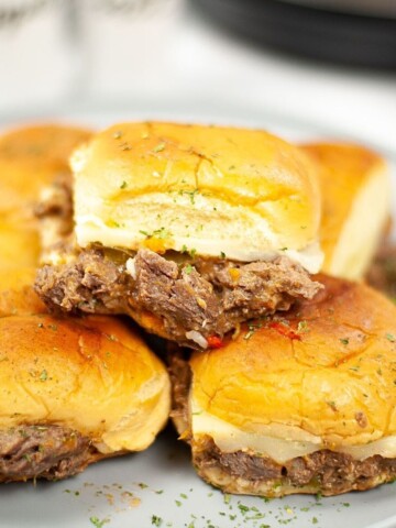 A stack of Philly cheesesteak sliders on a plate.
