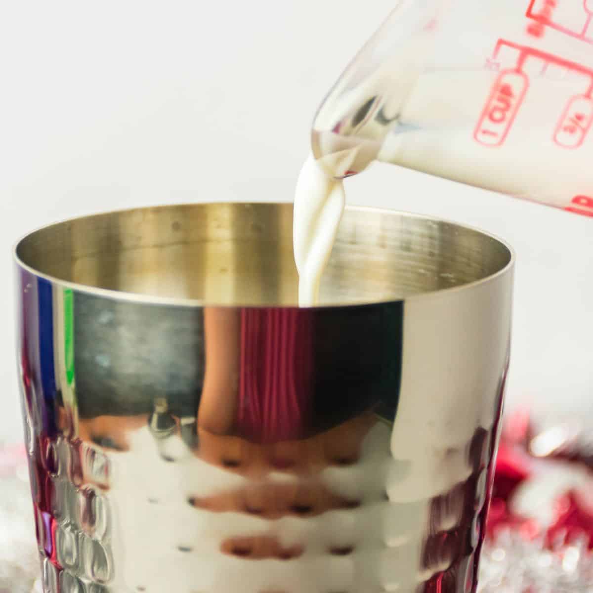 A cocktail shaker with a cream being poured into it.