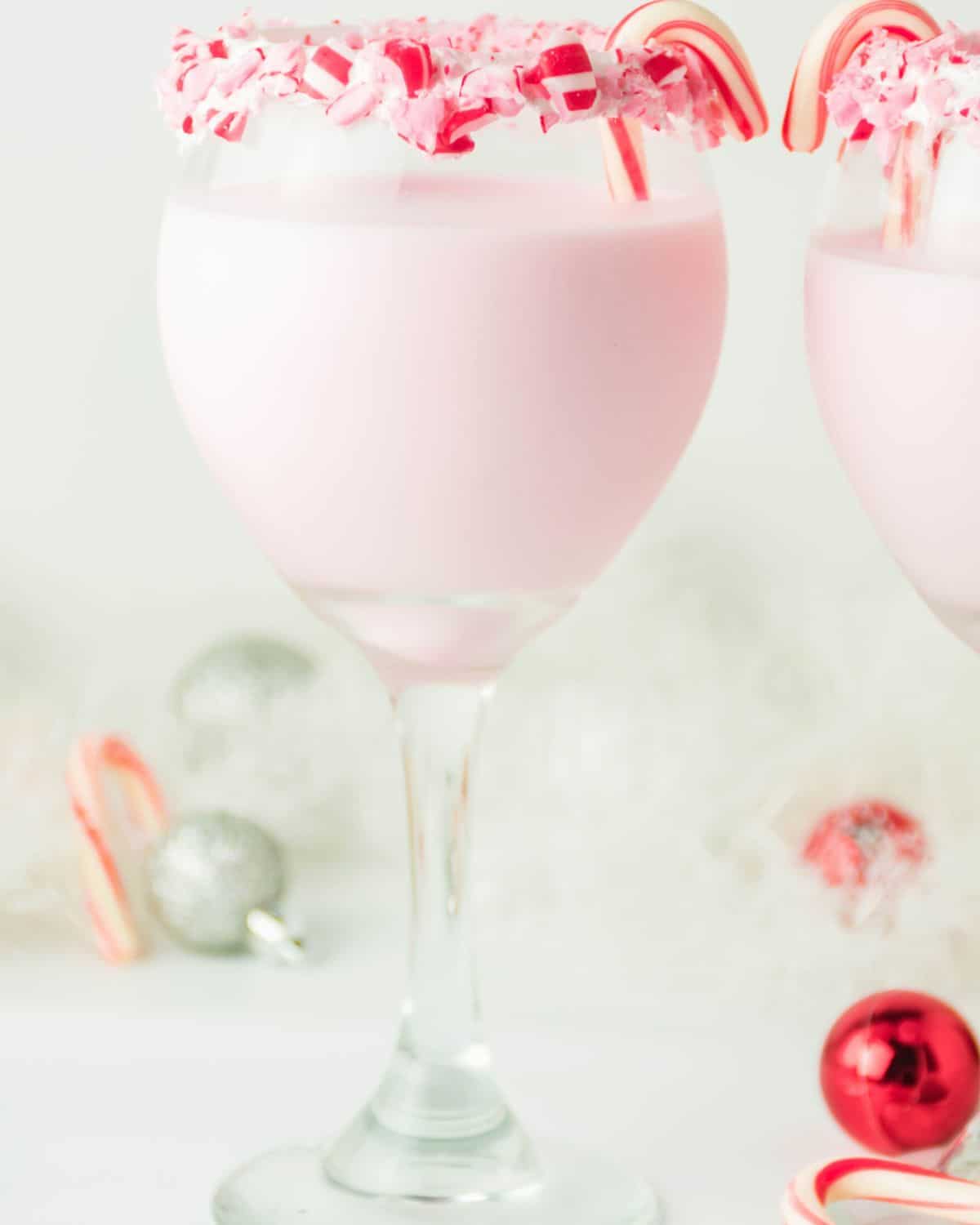 A glass of a pink cocktail with a rim of candy canes.