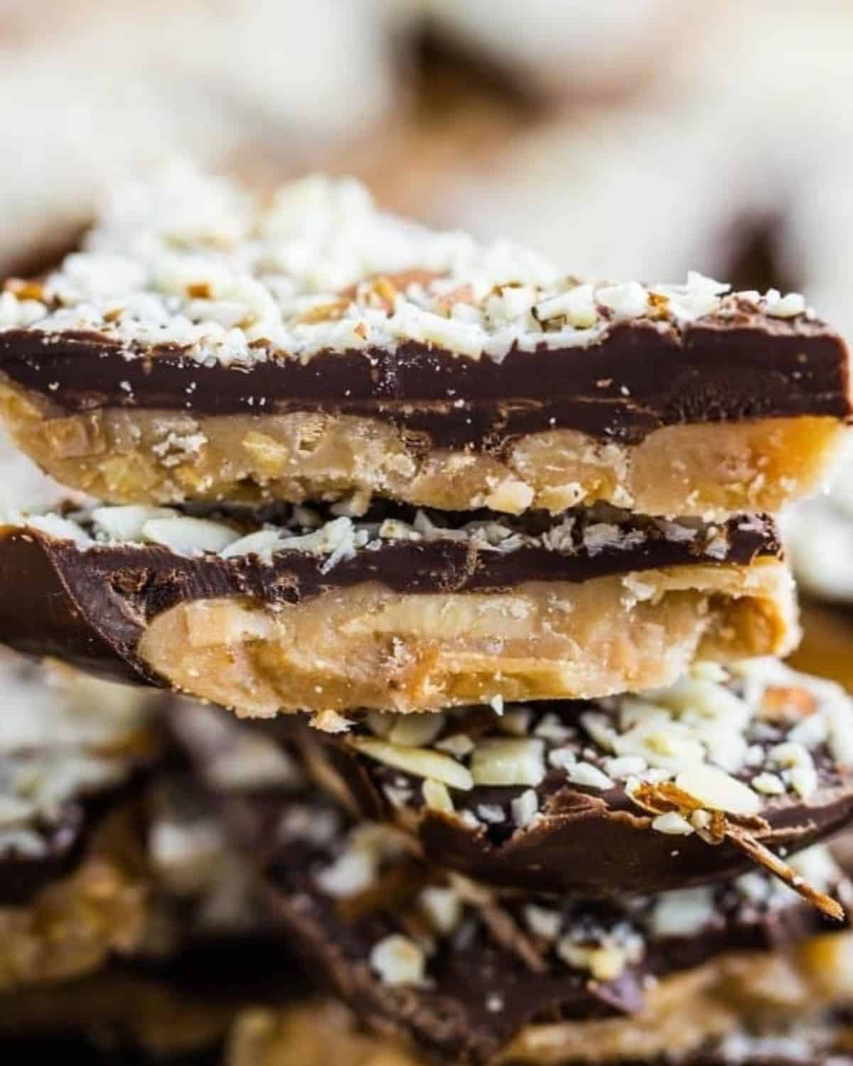 Pieces of almond roca candy stacked up and topped with pieces of almonds.