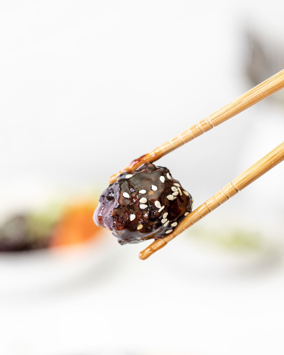 An asian meatball with sesame seeds held in chopsticks. 