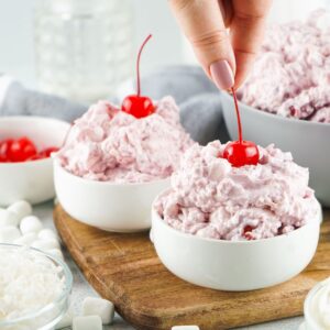 Two bowls of cherry fluff topped with cherries on a cutting board.