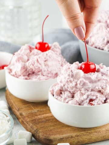 Two bowls of cherry fluff topped with cherries on a cutting board.
