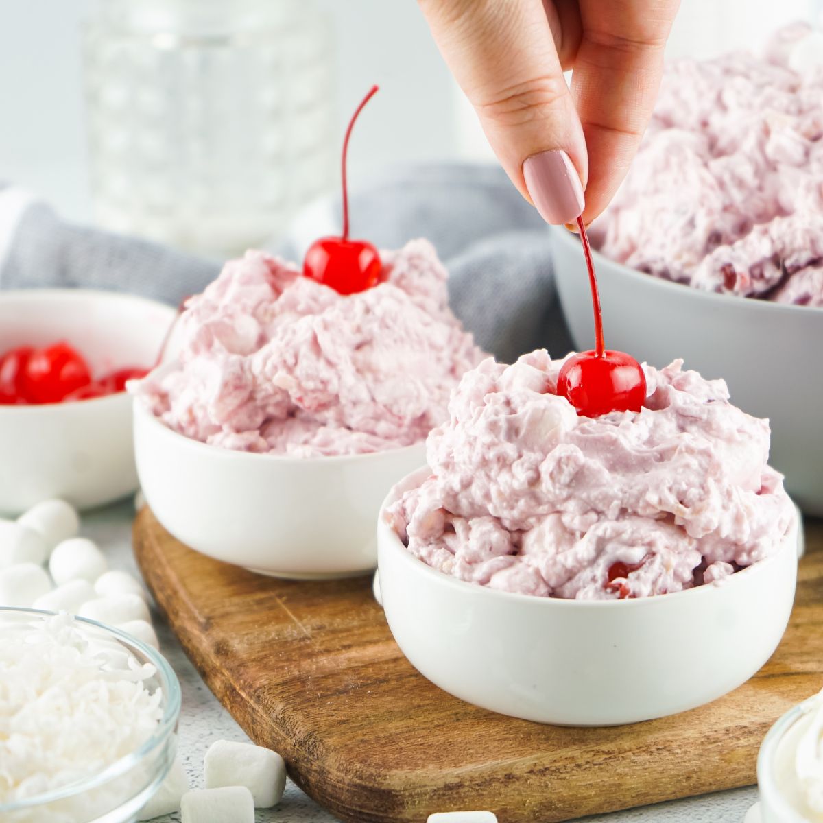 Two bowls of cherry fluff topped with cherries on a cutting board.