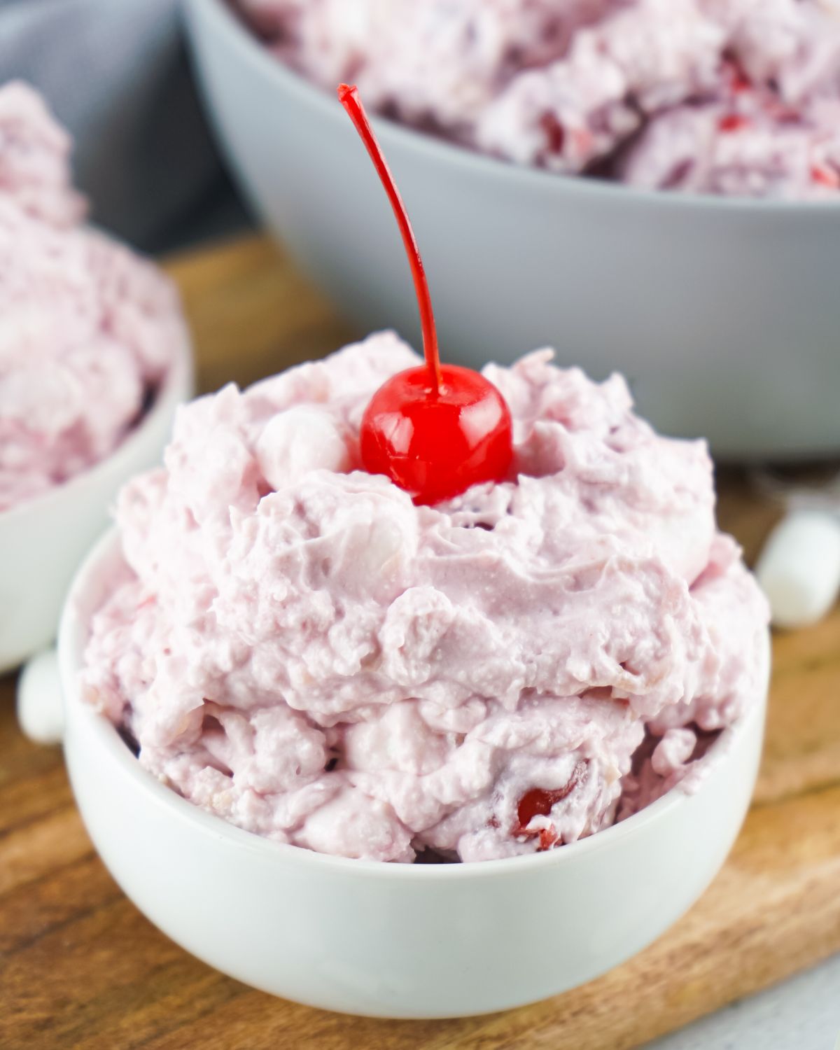 A bowl of light pink cherry fluff topped with a cherry. 