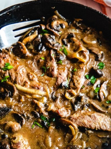 A cast iron pan with strips of cube steaks in a brown mushroom gravy.
