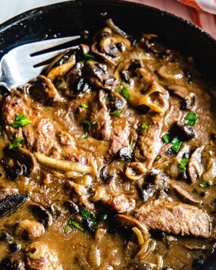A cast iron pan with strips of cube steaks in a brown mushroom gravy.