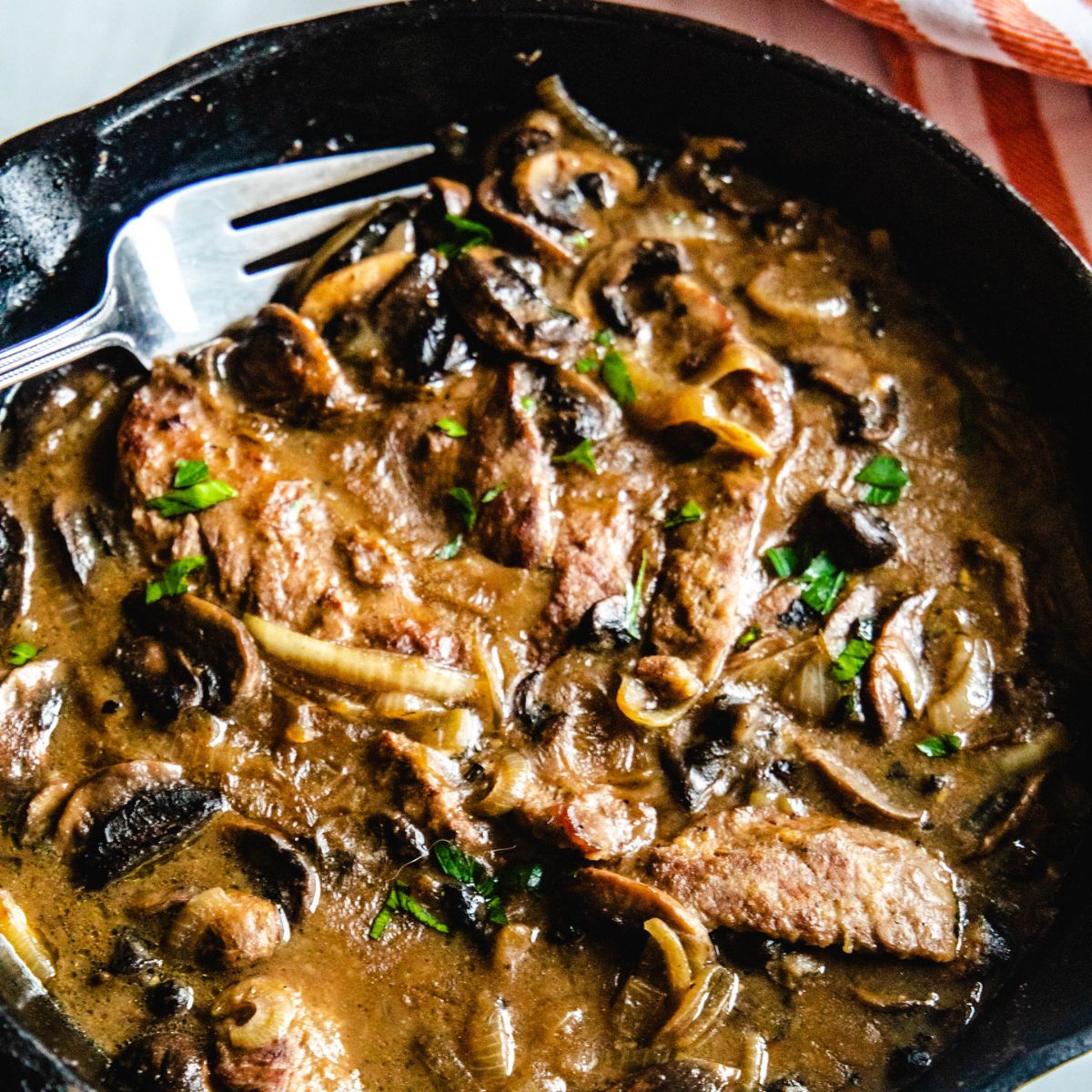 A cast iron pan with strips of cube steaks in a brown mushroom gravy.