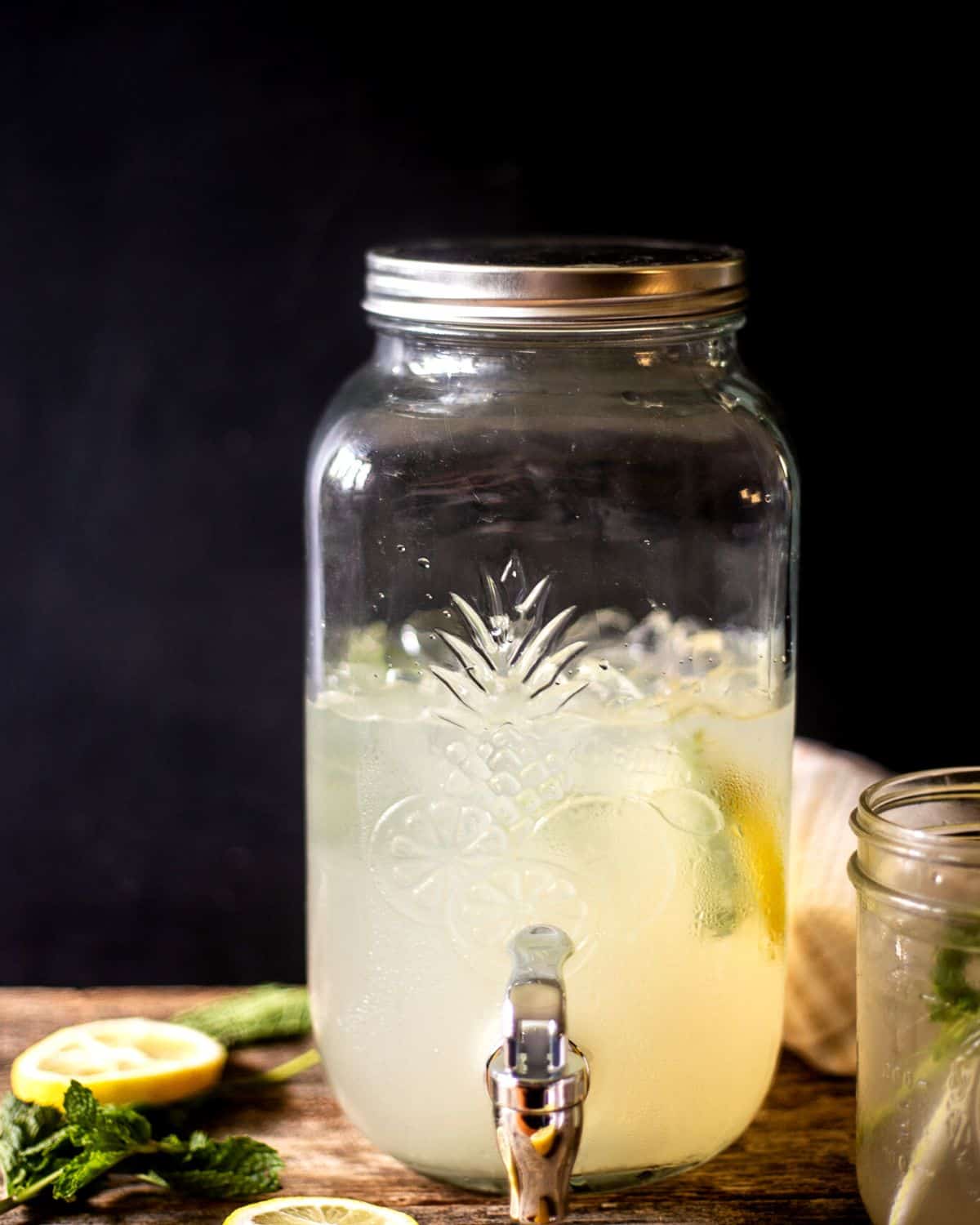 A large glass jar with a spout filled with ginger lemonade and mint. 