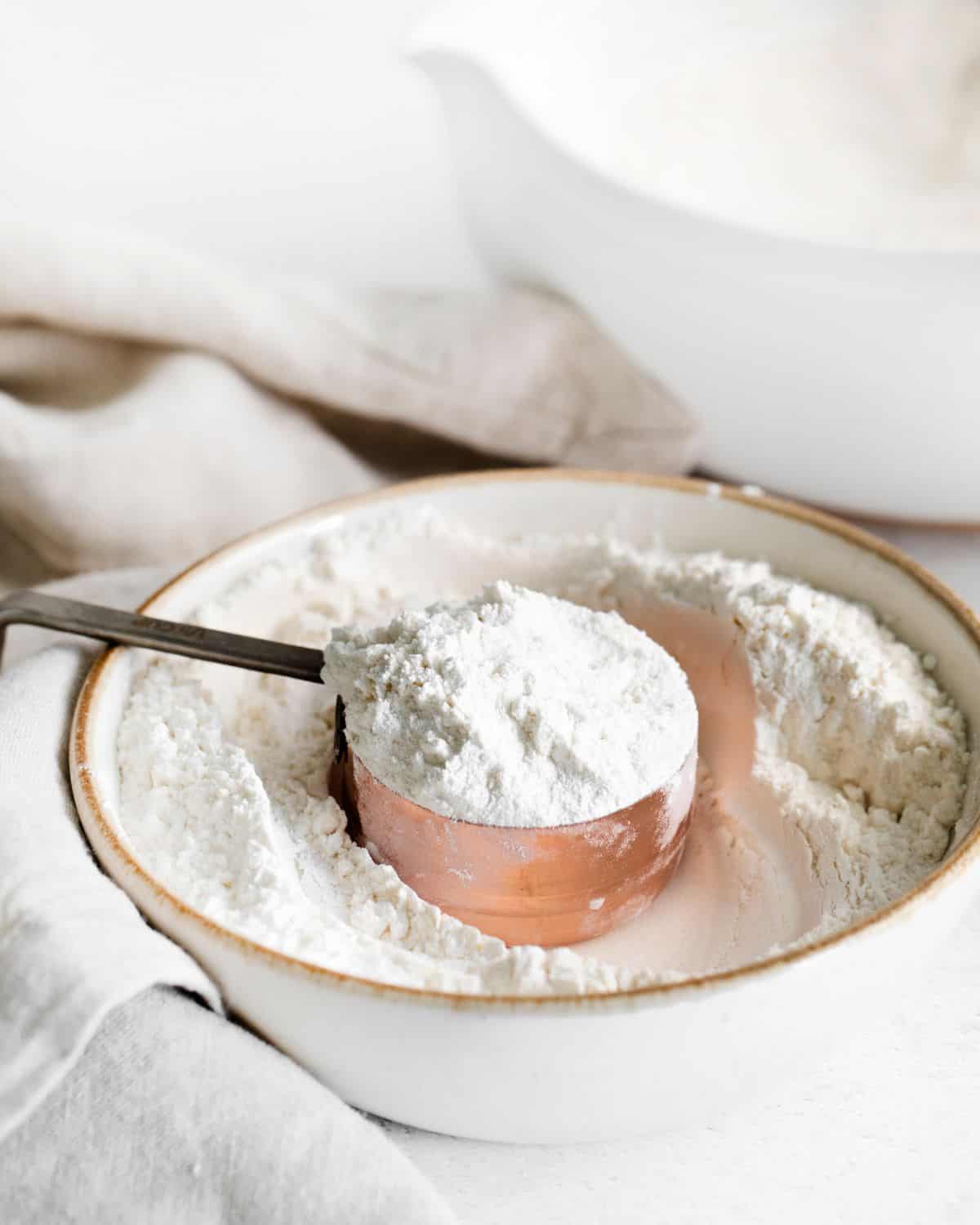 A measuring cup in a bowl of cake flour.