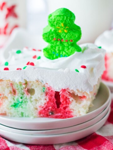 A white poke cake with red and green jello topped with a green peep.