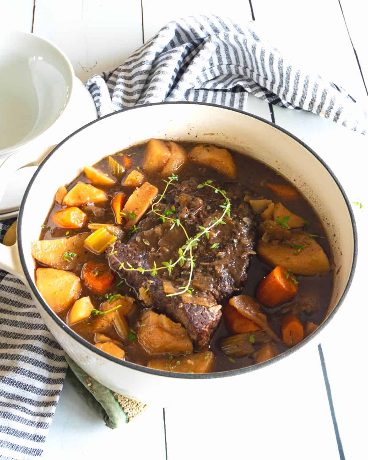 A white dutch oven with a pot roast, potatoes, and carrots in the pot. 