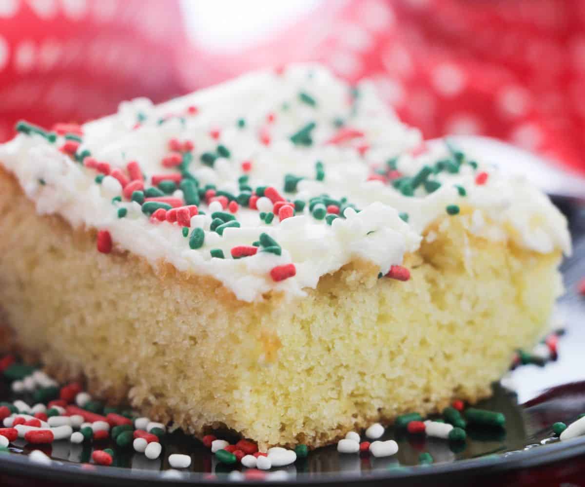 A slice of sugar cookie cake with white frosting and colored sprinkles.