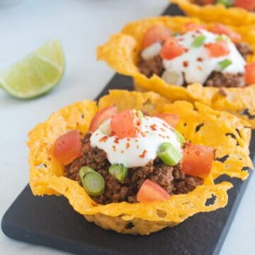 A low-carb cheese taco cup filled with taco meat and topped with sour cream and tomatoes.