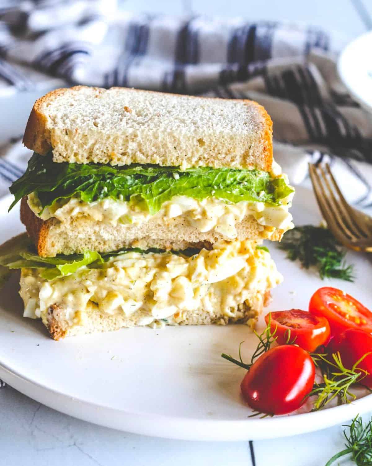 An egg salad sandwich stacked on a plate with lettuce.
