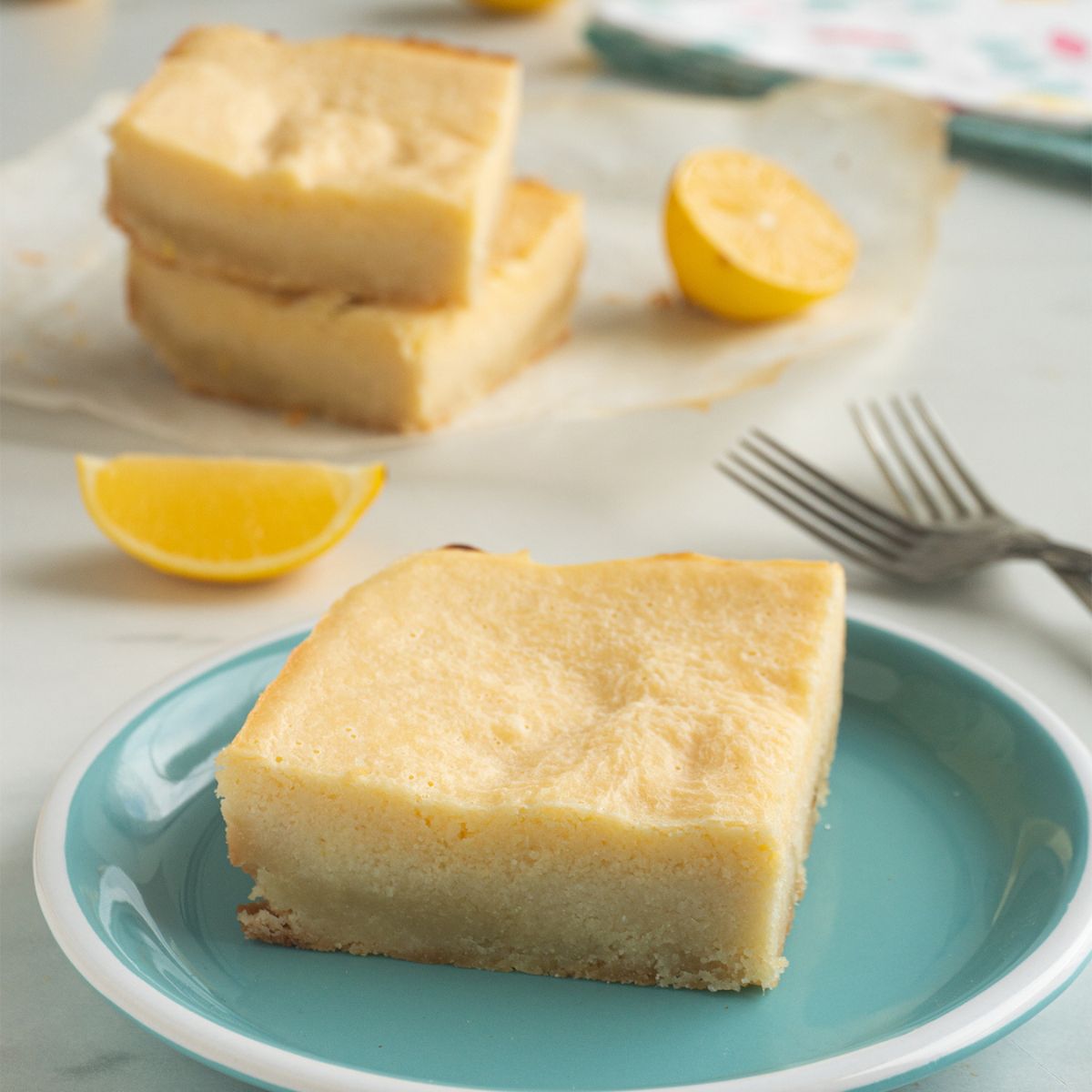 A green plate with keto lemon bars on the plate with a stack of lemon bars behind them.