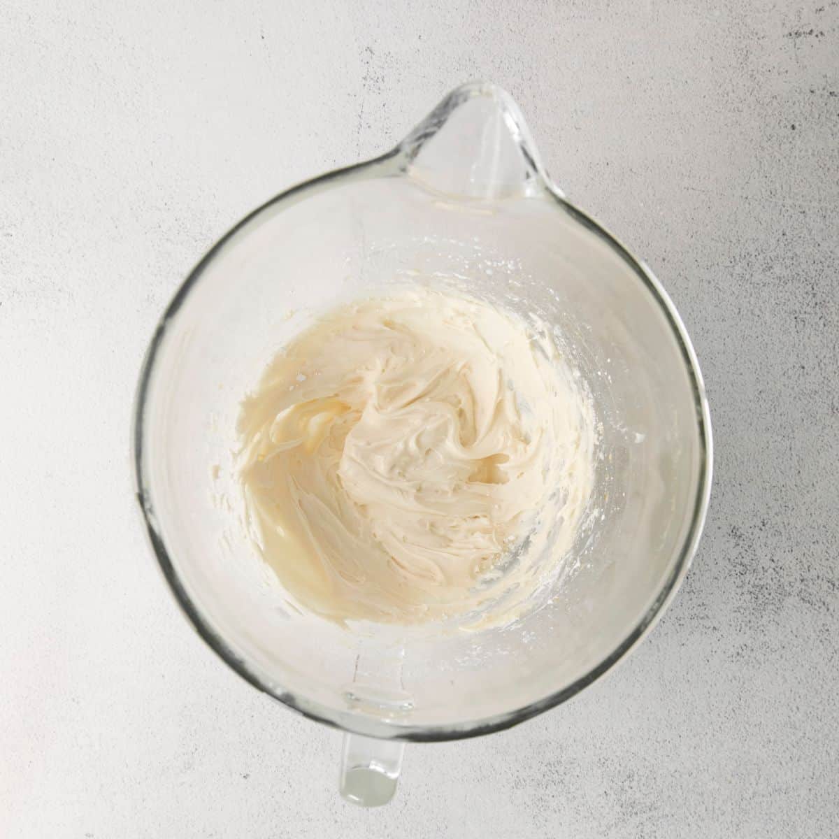 A glass mixing bowl with maple buttercream frosting in the bow.