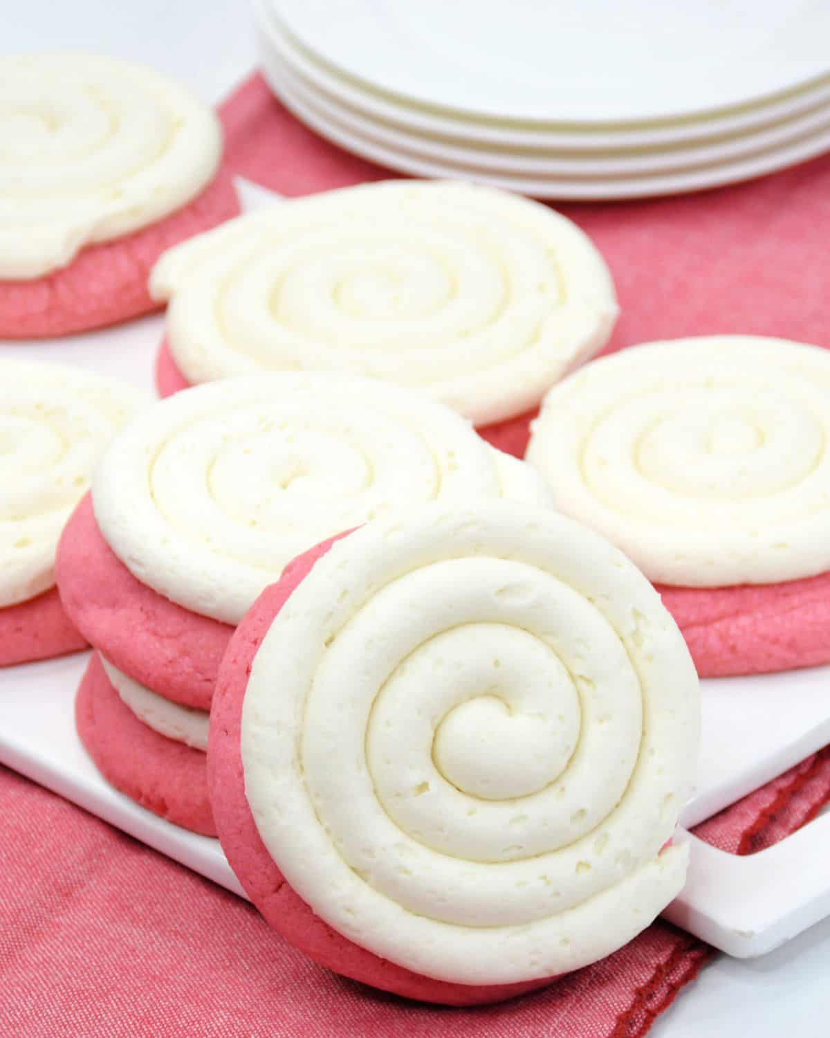 A stack of copycat crumbl pink velvet cookies with frosting. 