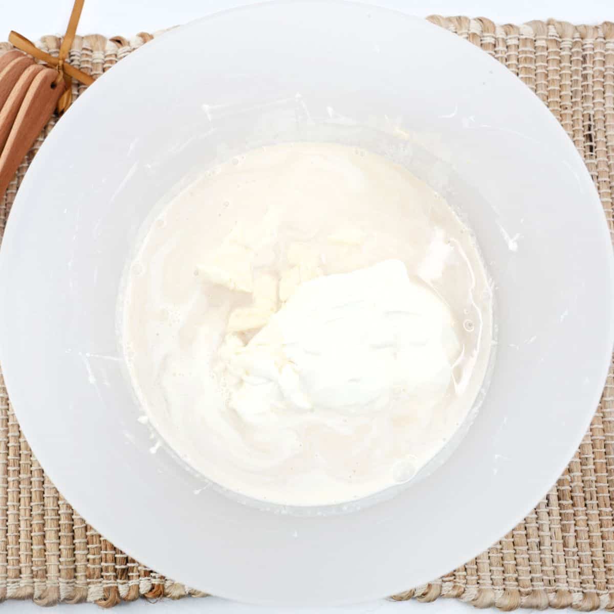 A white bowl with cream cheese, confectioners' sugar, and vanilla extract. 
