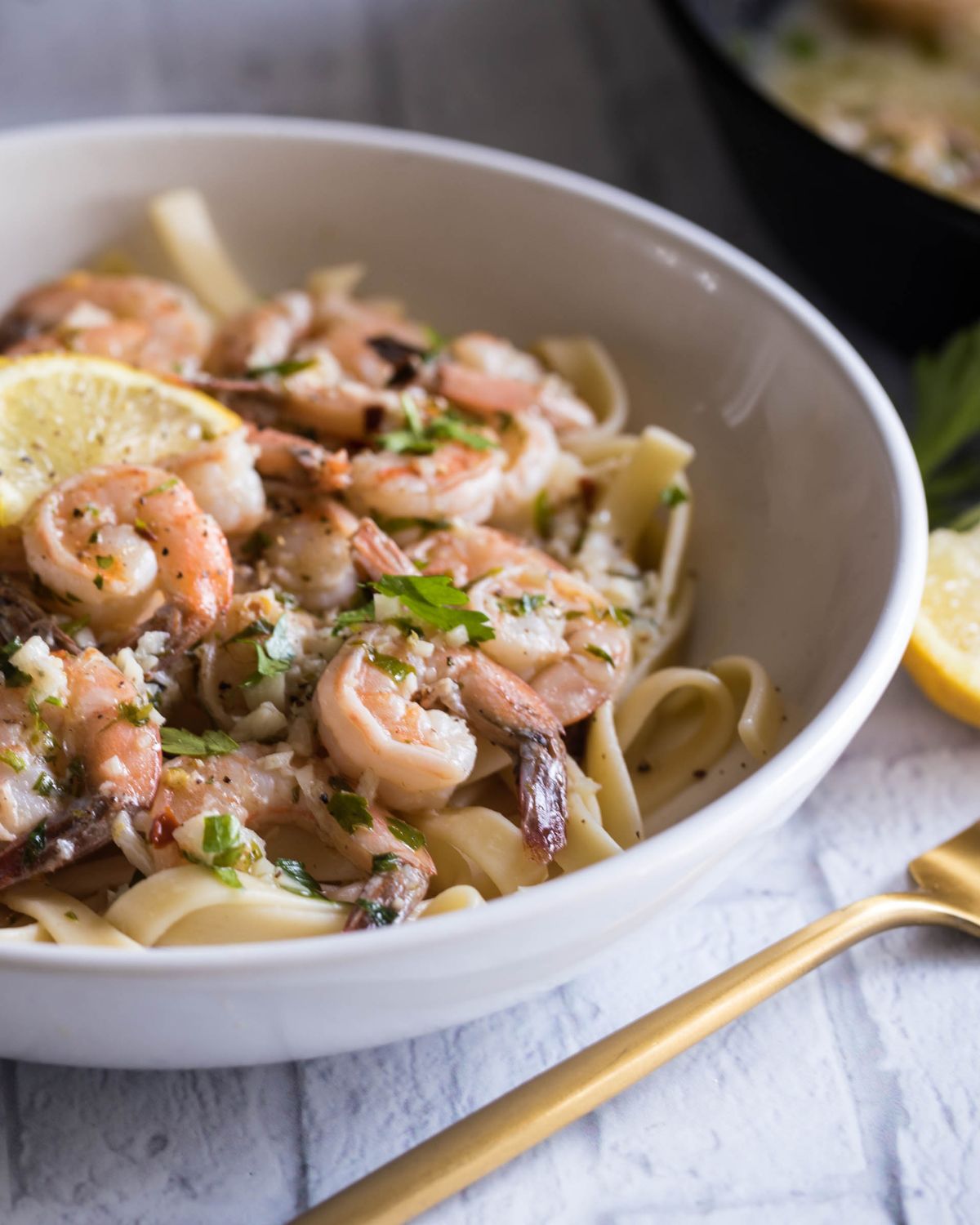 Shrimp scampi with lemons over pasta. in a white pasta bowl.
