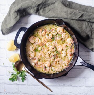 An overhead view of a cast iron pan with shrimp in garlic wine sauce.