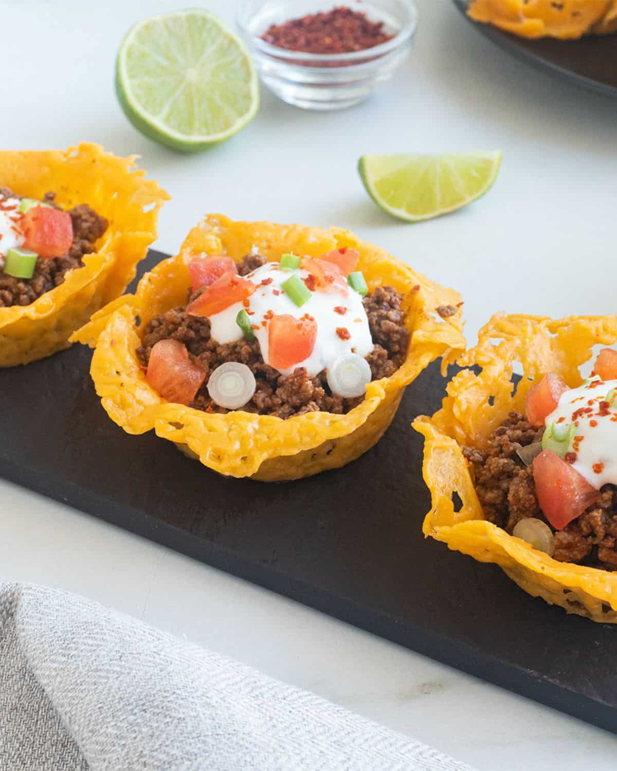 A black slate with taco cheese crisps filled with taco meat and toppings.