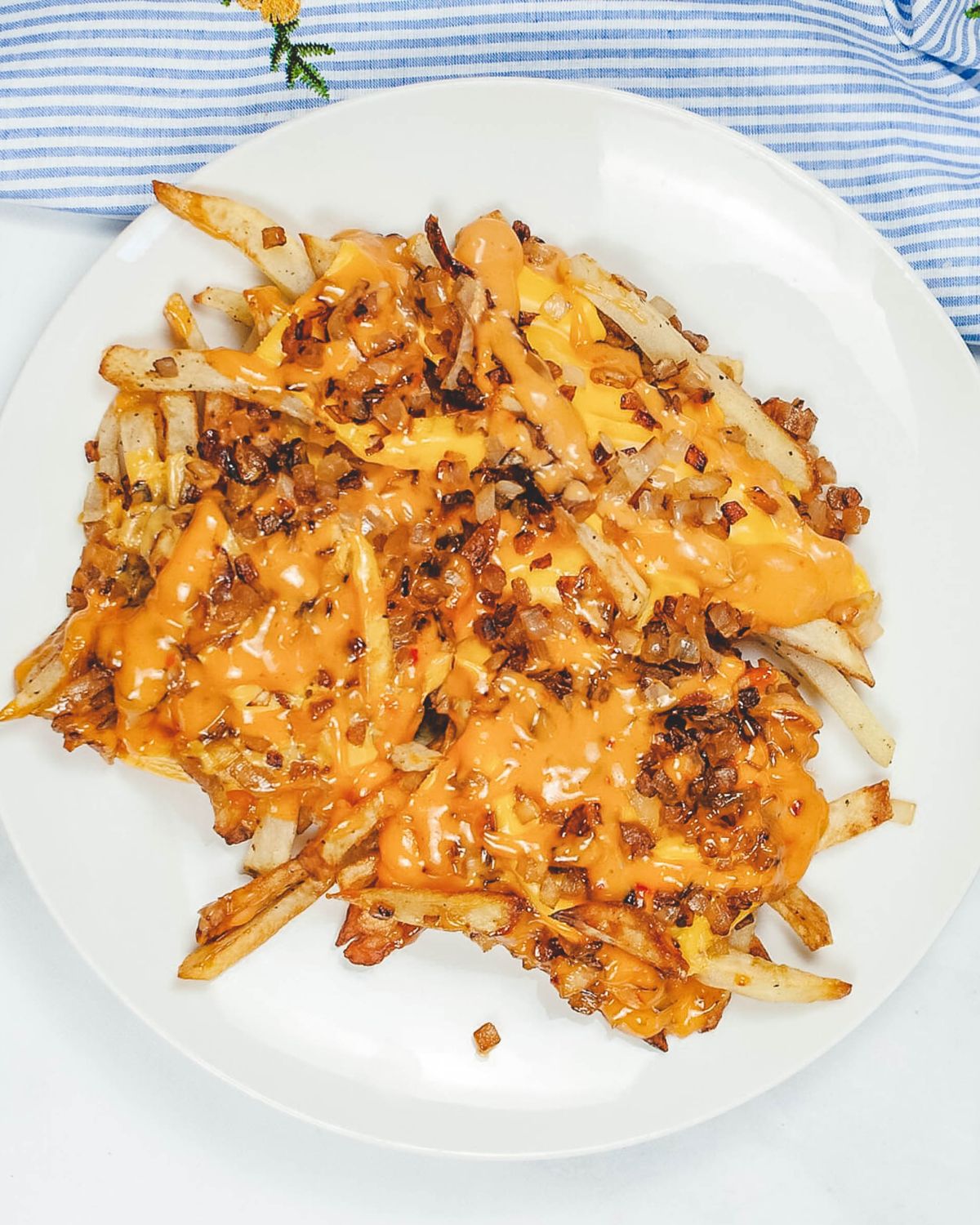 A white bowl filled with french fries topped with American cheese and fried onions.