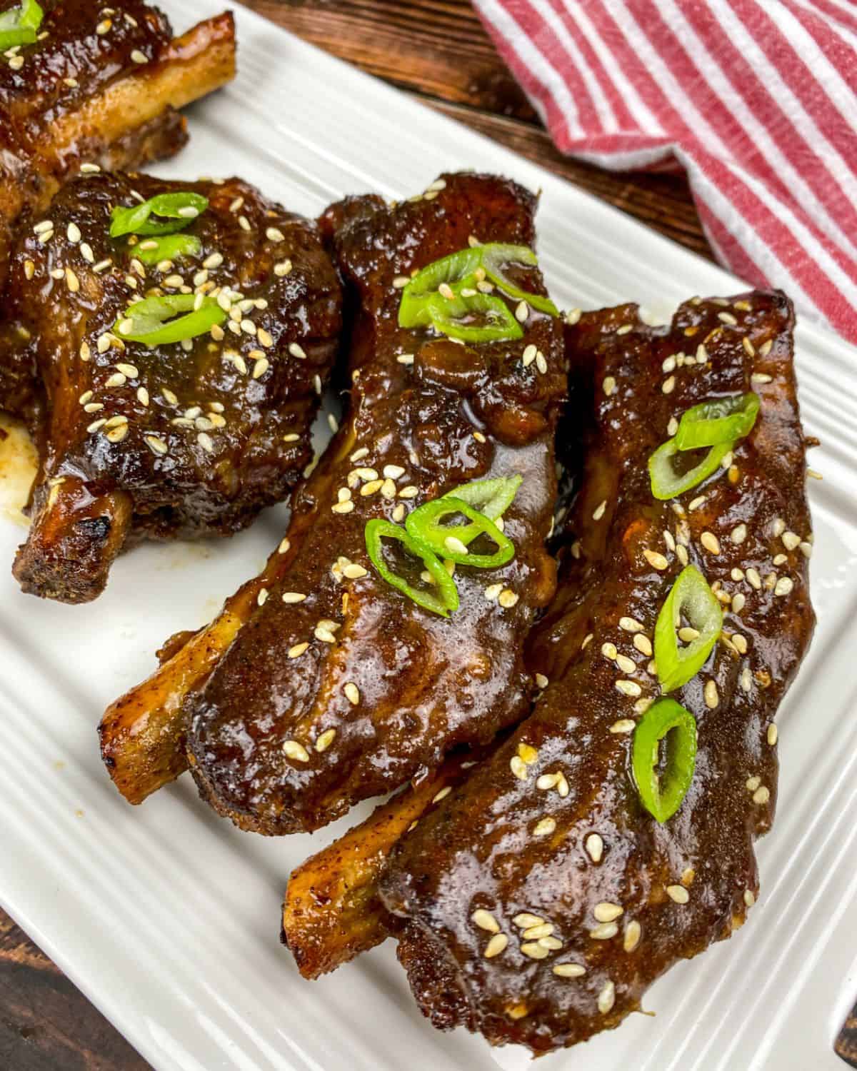 Asian Spare ribs with sesame seeds and green onion garnish on a plate. 