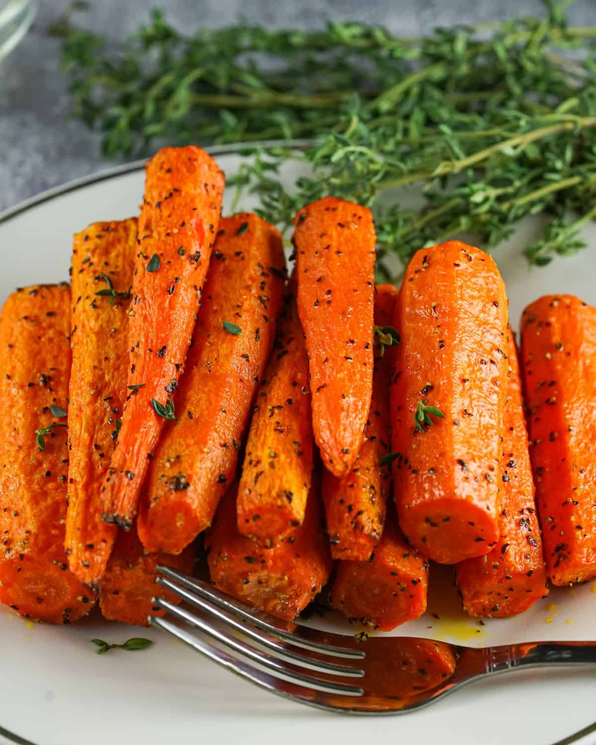 Air fryer carrots on a white plate with fresh thyme in the back of the plate.