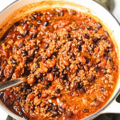 A white Dutch oven filled with a big pot of chili made with adobo chipotle peppers and ground beef.