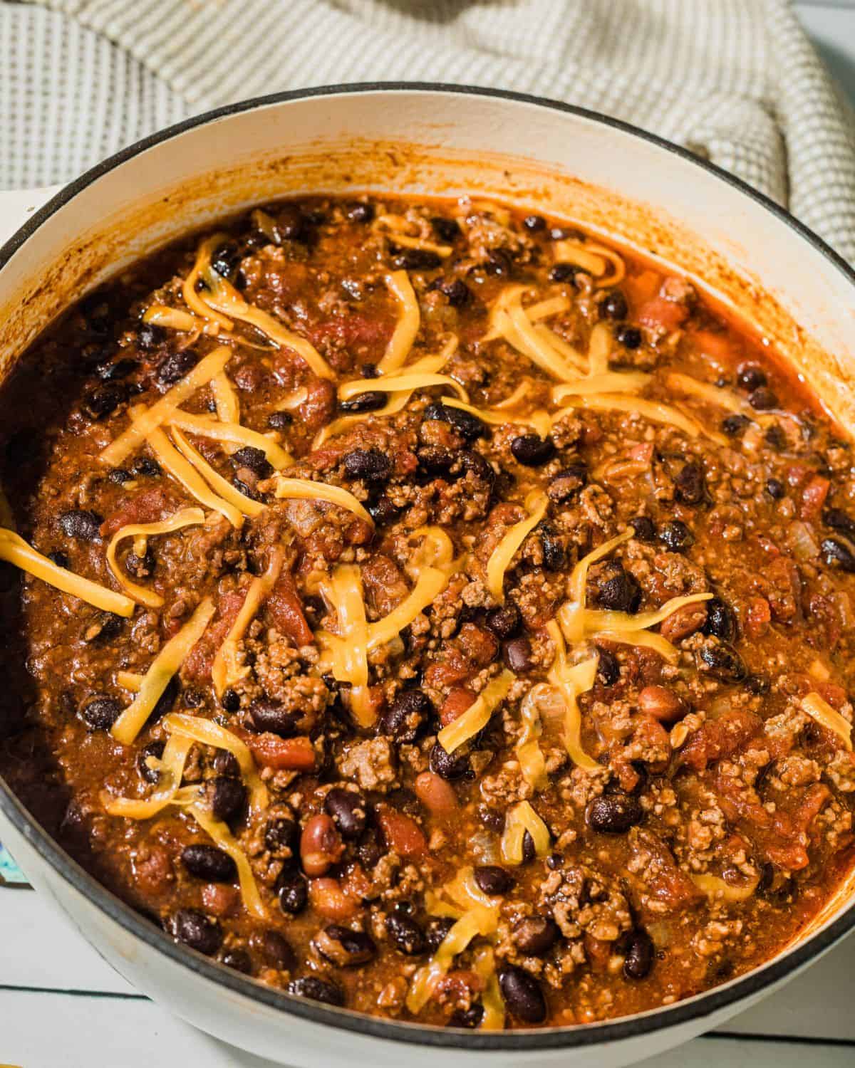 A Dutch oven with chipotle chili topped with shredded cheddar cheese.