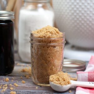 A mason jar filled with homemade light brown sugar with a teaspoon of brow sugar in front of the jar.