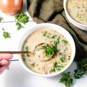 A big spoon of potato, kale, and ground sausage cooked in a soup of zuppa toscana.