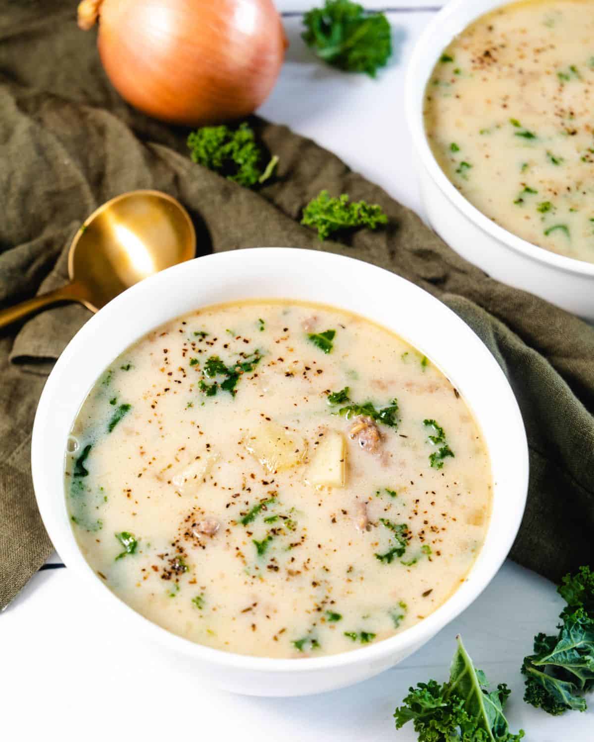 A white soup bowl filled with creamy zuppa toscana with kale.