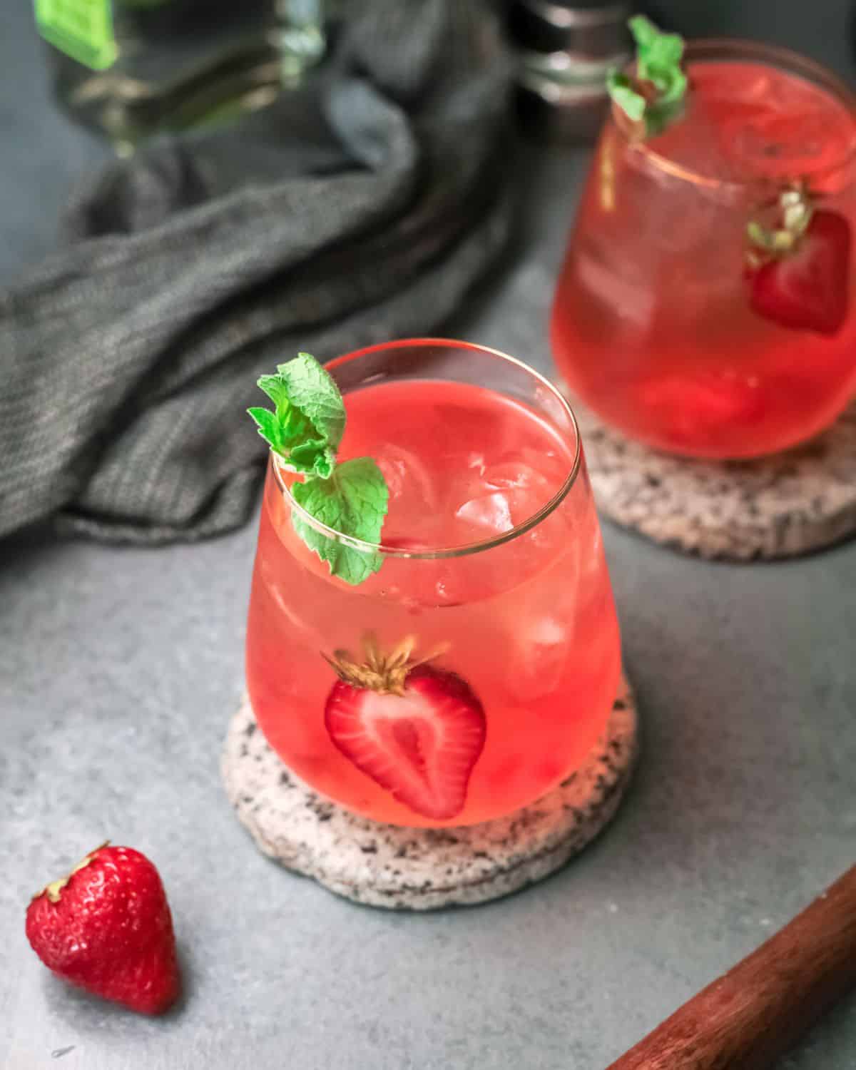 Two glasses with a light blush colored beverage with mint and strawberries.