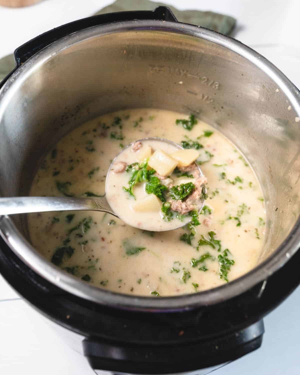 An instant pot filled with a creamy soup with kale, ground sausage, and potatoes. 