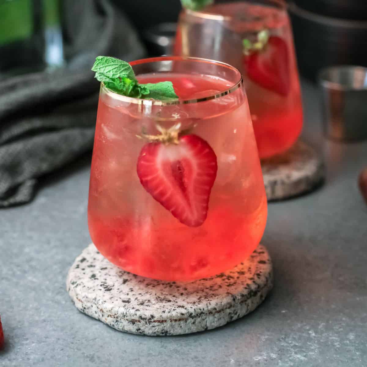 Strawberry Paloma cocktails on speckled coasted with sliced strawberry and mint for garnish.