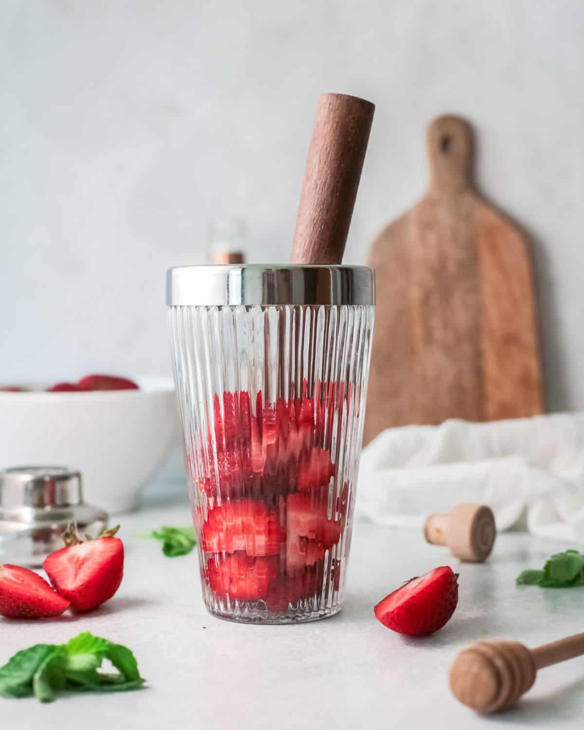 Strawberries in a cocktail shaker being muddled for a Paloma.