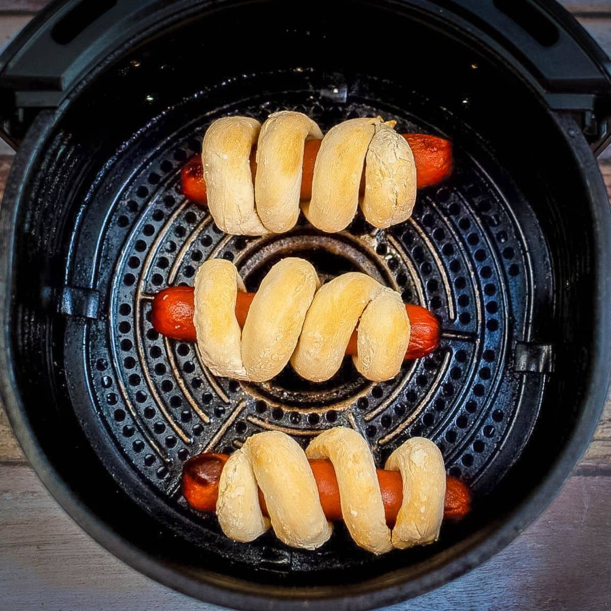 Cooked hot dogs in pretzel buns in the basket of the air fryer.