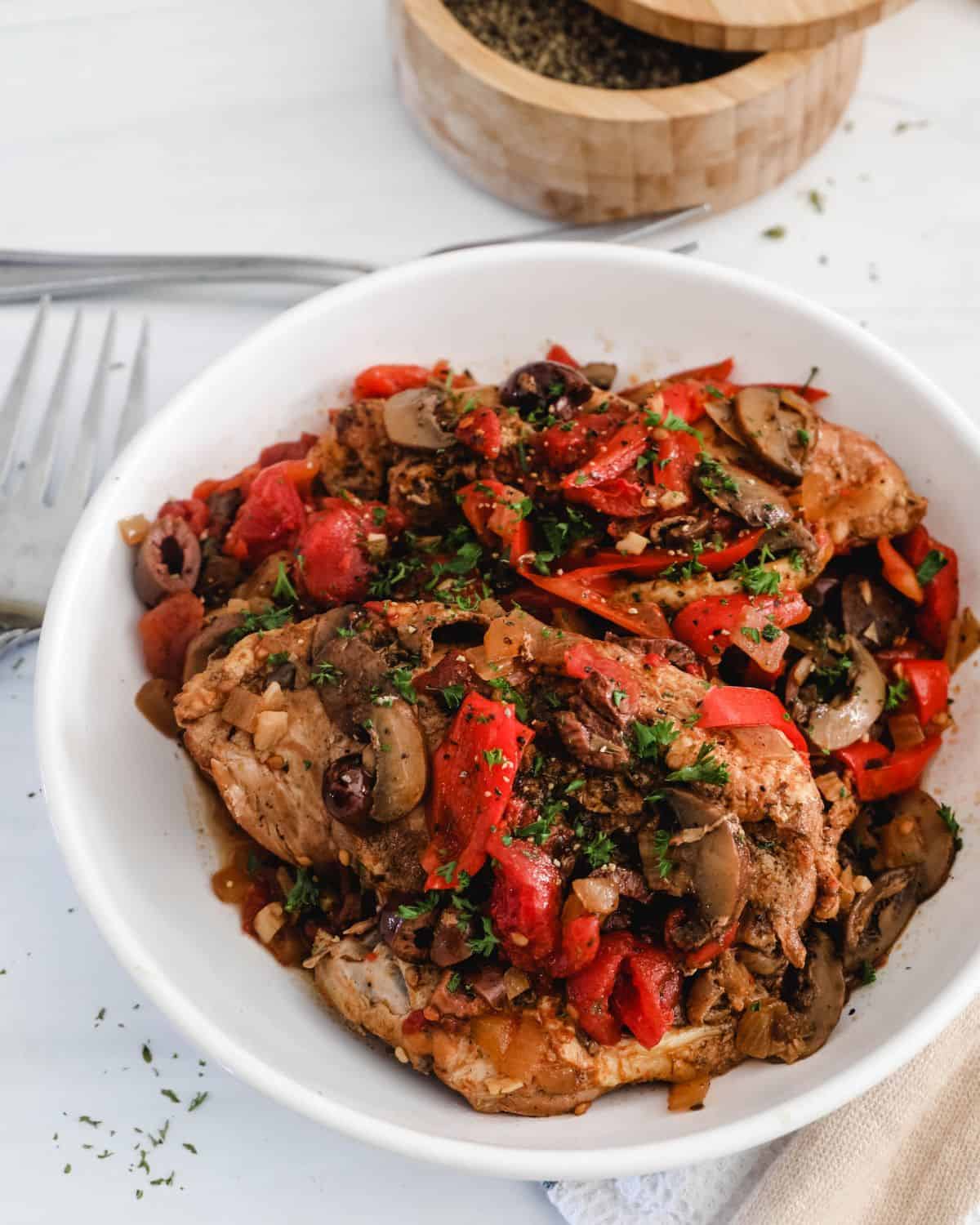 A white bowl with chicken cacciatore, peppers, and mushrooms.