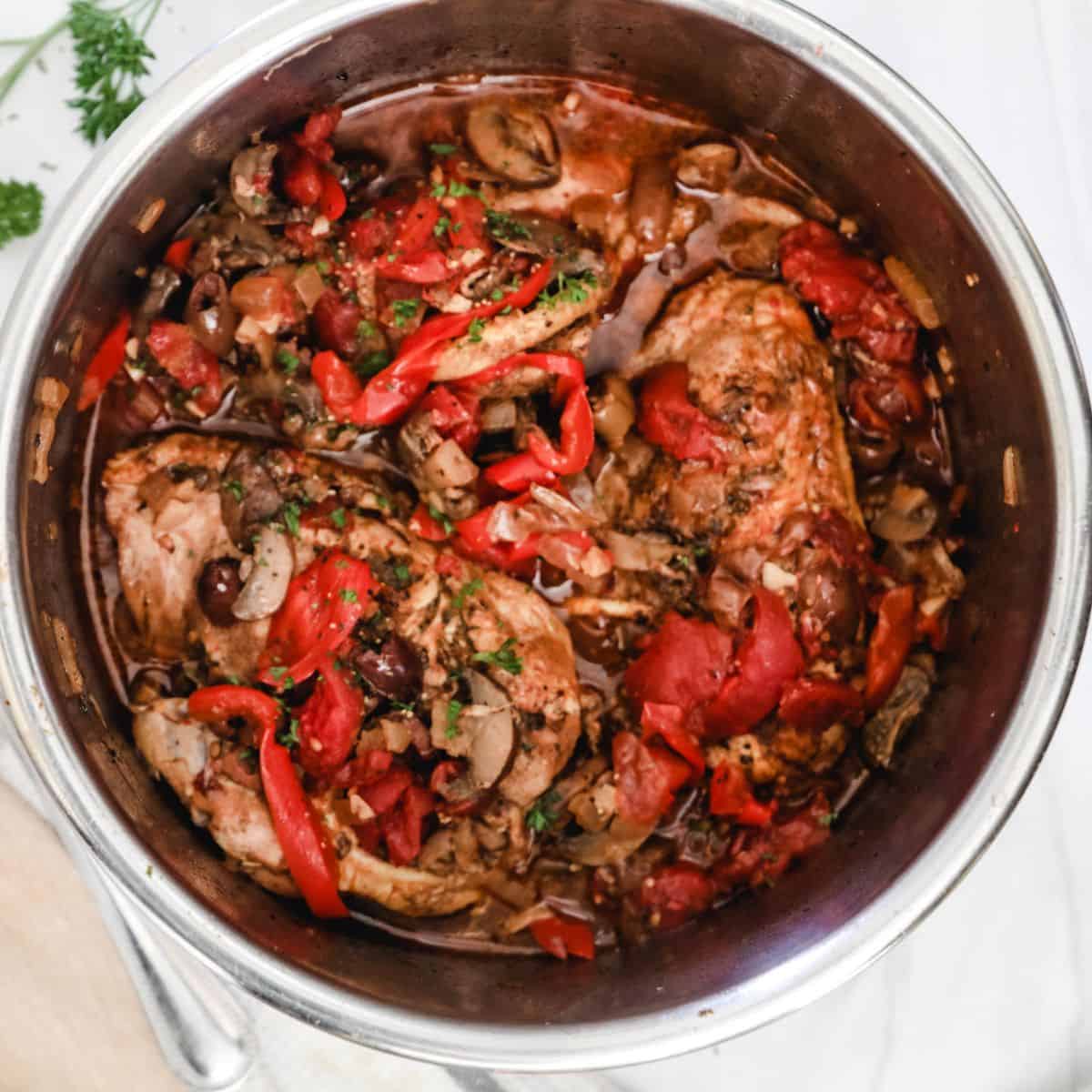 The cooking vessel for chicken cacciatore is filled with cooked chicken, pepper, and mushroom.