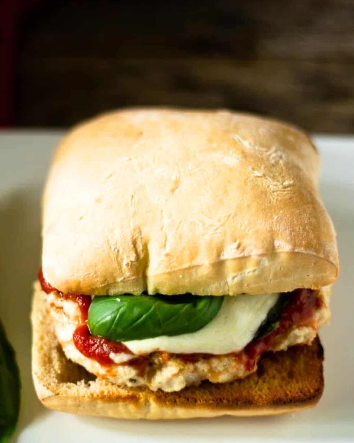 A chicken parmesan burger with fresh basil, marinara sauce, and mozzarella on an Italian ciabatta roll.