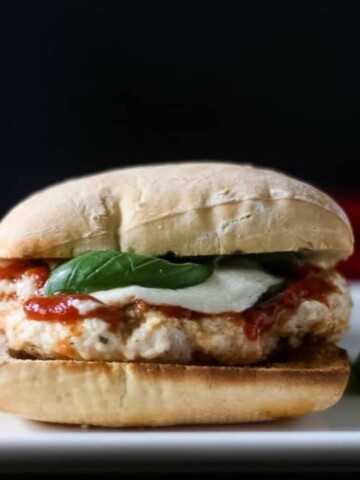 A side view of a ciabatta roll with a chicken parm patty on it.